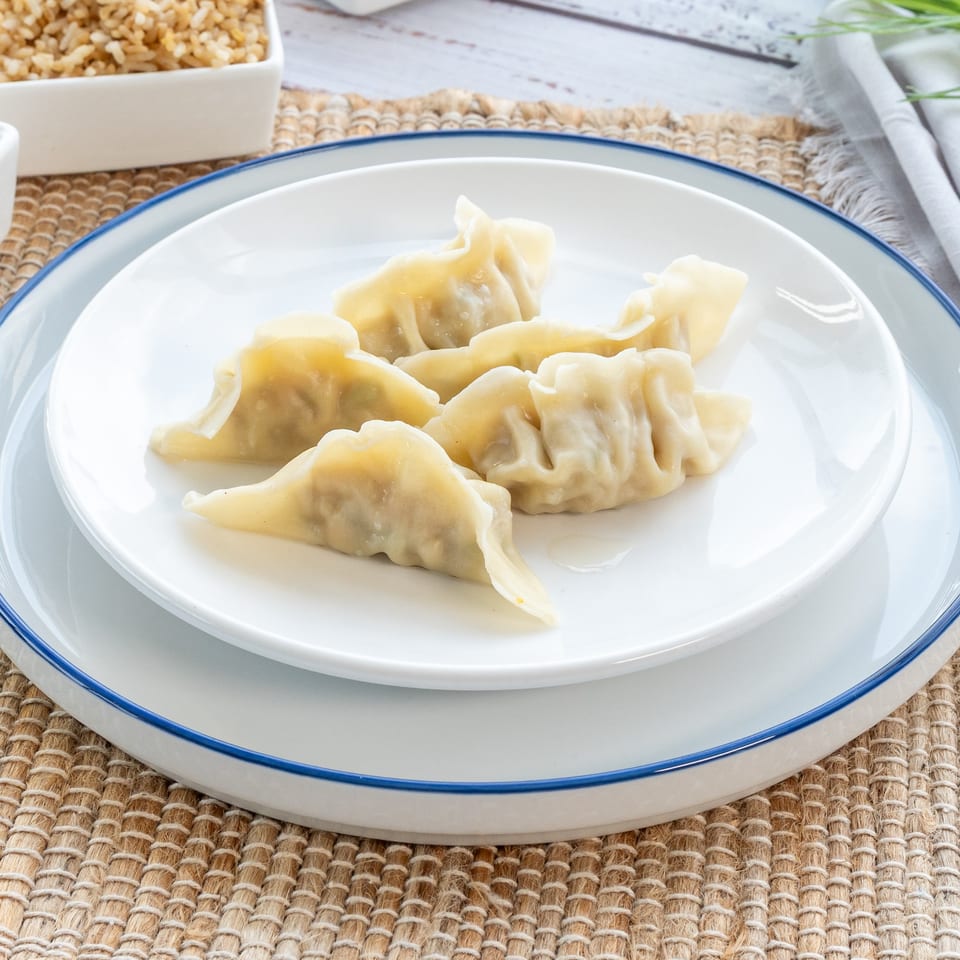 Six steamed dumplings, likely pork or vegetable, on a white plate with a blue rim, ready to be served.