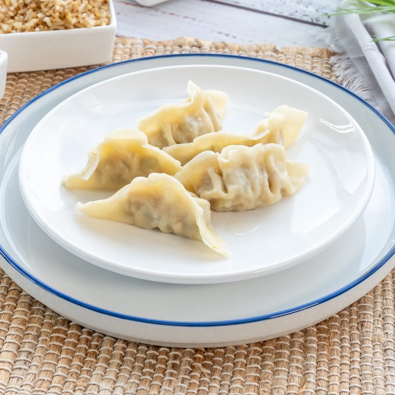 Six steamed dumplings, likely pork or vegetable, on a white plate with a blue rim, ready to be served.