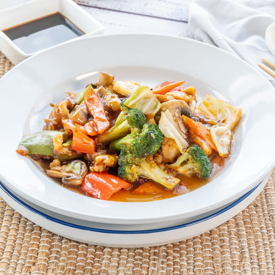 A white plate filled with colorful Chinese stir-fry, featuring broccoli, bell peppers, and mushrooms.