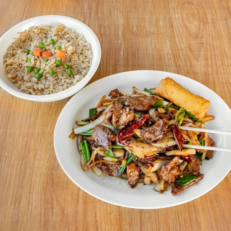 Spicy beef stir-fry with onions, green onions, and red chilies, served with fried rice and an egg roll.