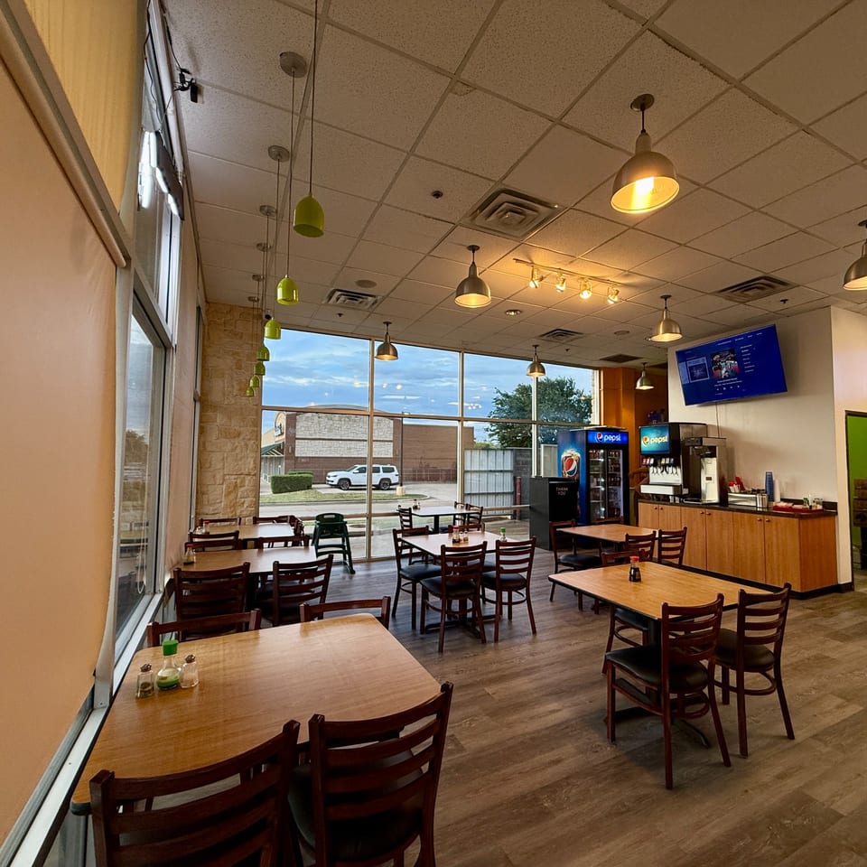 Interior of Red Panda Wok & Grill with empty tables, chairs, large windows, and a drink station.