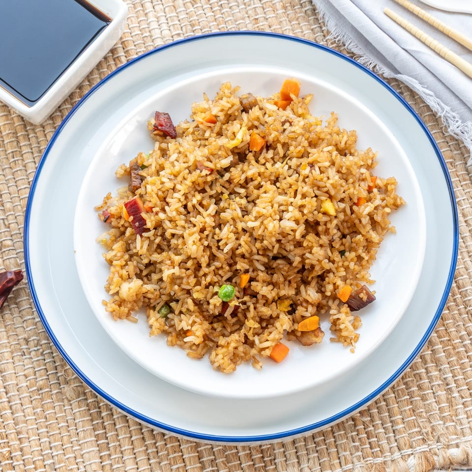 A white plate with blue rim holds a generous serving of Red Panda Wok & Grill's fried rice.