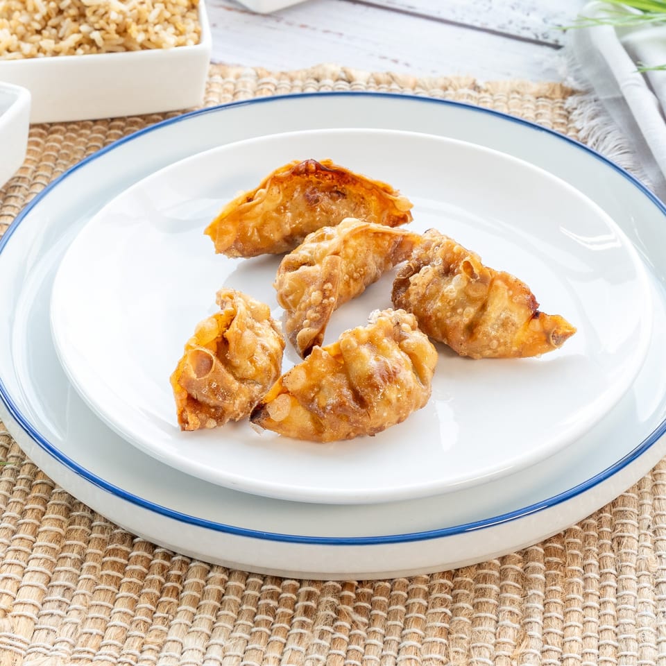 Six crispy fried dumplings, golden brown, arranged on a white plate with blue rim, next to fried rice.