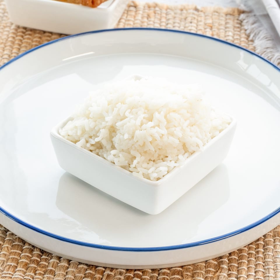 A small white square bowl filled with fluffy white rice, centered on a large white plate.